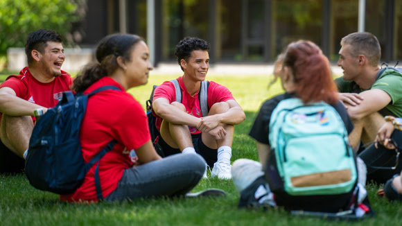 Group of students with backpacks sitting in a circle on grass