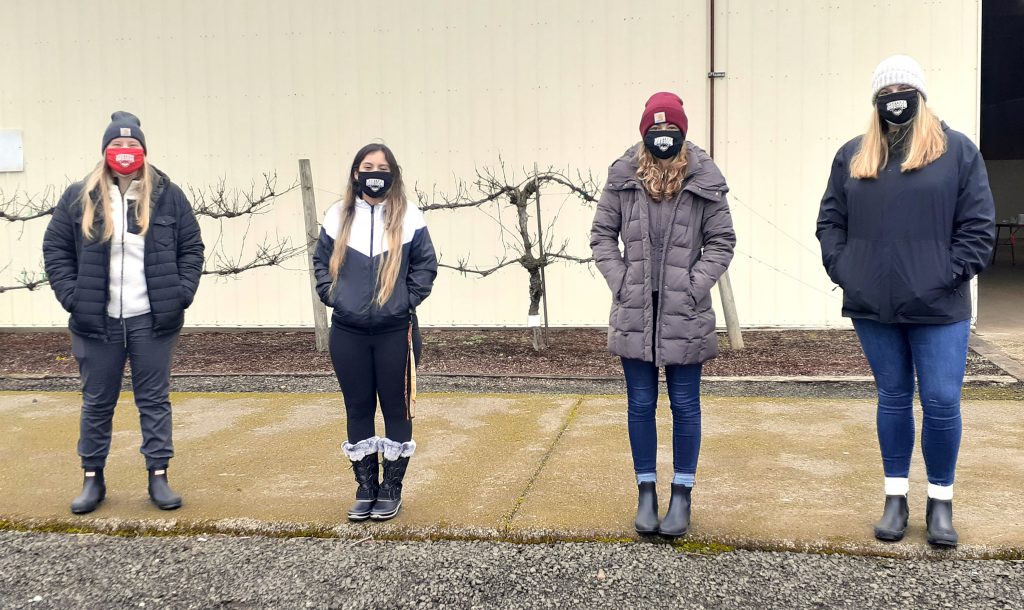 Contact tracing team Four students wearing WOU non-surgical masks stand in front of a warehouse.