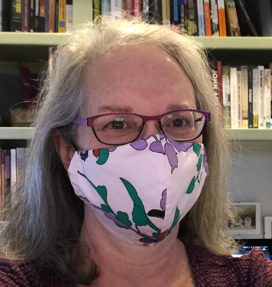 mask selfie - Sue Sue Monahan wearing a non-surgical mask in front of shelves of books