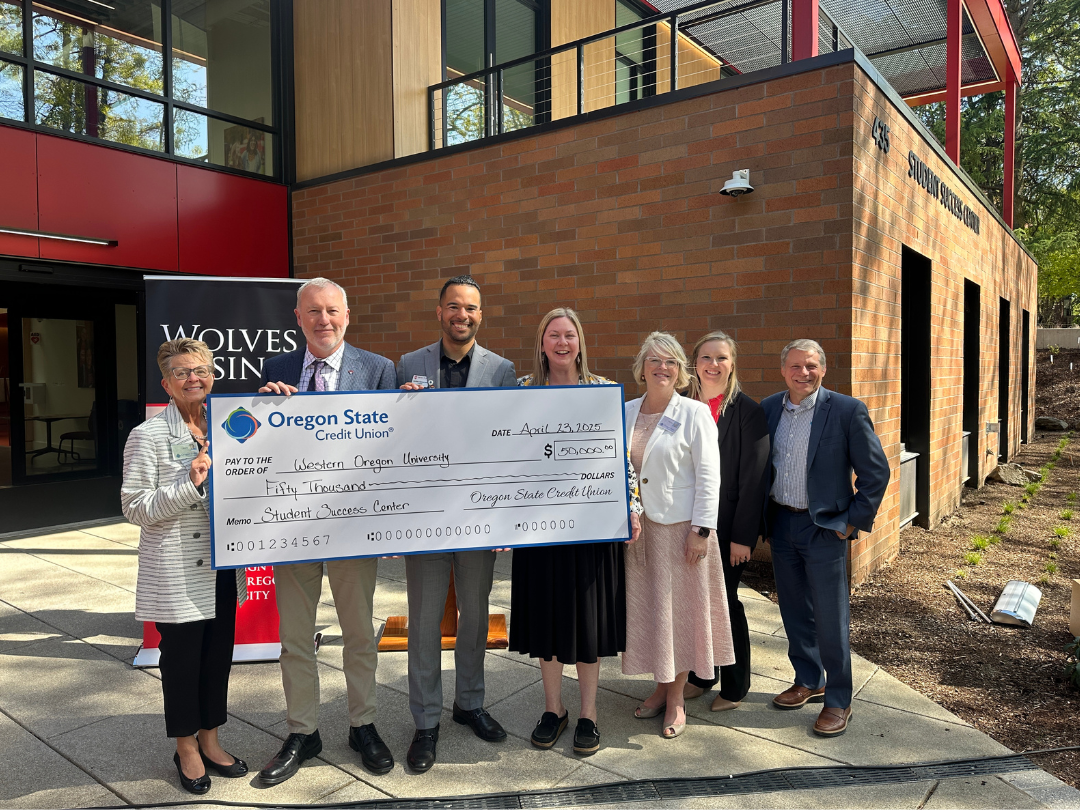 image of 7 people standing in a line holding a check in front of a brick building